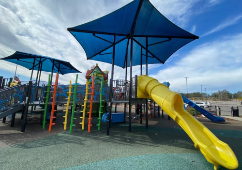 Colorful playground with slides and climbing structures under blue canopies, set against a cloudy sky.
