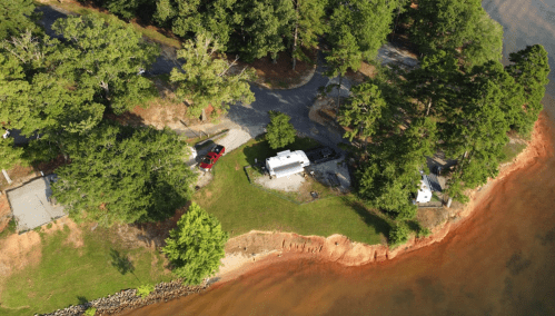 Aerial view of a lakeside campsite with RVs, surrounded by trees and a sandy shoreline.