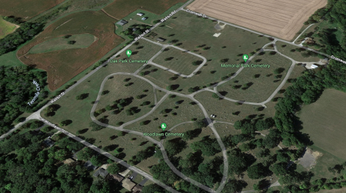 Aerial view of a cemetery area with multiple winding roads and green spaces, surrounded by fields and trees.