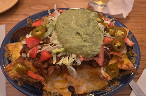 A plate of nachos topped with guacamole, chili, tomatoes, lettuce, and jalapeños.