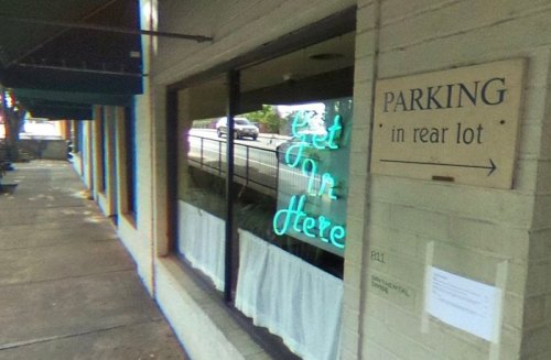 A storefront with a neon "Get In Here" sign and a parking sign indicating rear lot access.