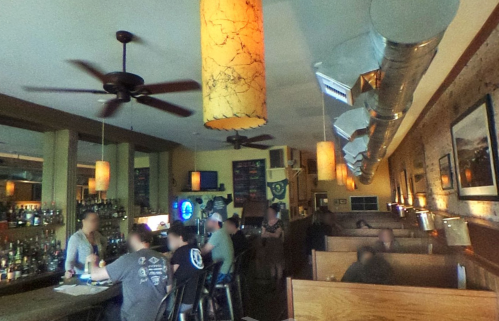 A cozy restaurant interior with wooden booths, a bar, and warm lighting, featuring patrons enjoying their meals.