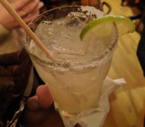 A close-up of a cocktail glass with a salted rim, filled with a light-colored drink and a lime wedge.