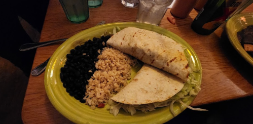 A vibrant plate featuring two tortillas, black beans, rice, and shredded lettuce on a wooden table.