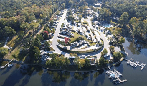 Aerial view of a lakeside campground with RVs, trees, and a marina, surrounded by water and autumn foliage.