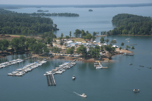 Aerial view of a marina with boats, docks, and a lakeside area surrounded by trees and water.