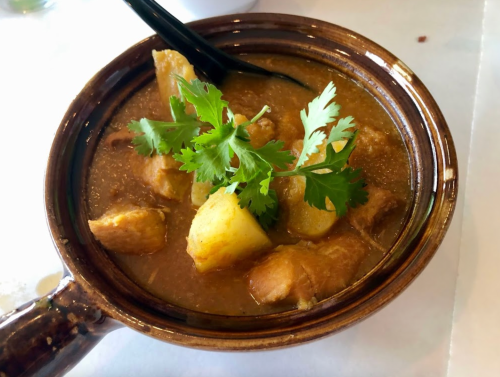 A bowl of stew with potatoes and meat, garnished with fresh cilantro, served with a black spoon.
