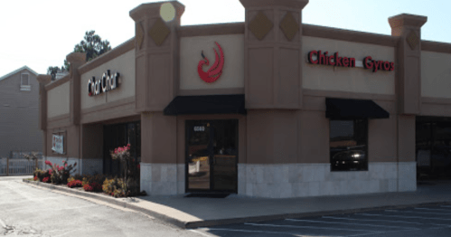 Exterior of a restaurant featuring a sign for "Chicken Gyros" and a decorative facade, with flowers in front.