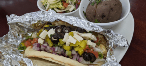 A foil-wrapped sandwich filled with vegetables and cheese, served with two bowls of salad and black beans.