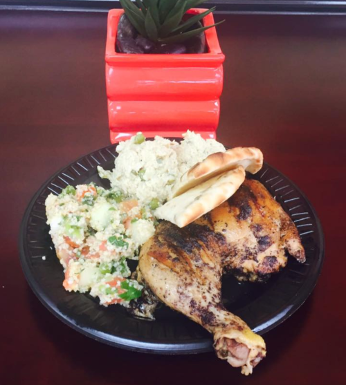 A plate with grilled chicken, a side of vegetable rice, and two small pita breads, with a small plant in a red pot.