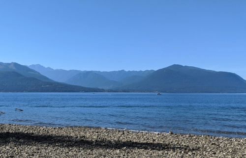A serene lake scene with mountains in the background and a rocky shoreline under a clear blue sky.