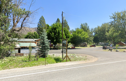 A scenic view of a rural road intersection with trees, a sign, and parked vehicles under a clear blue sky.