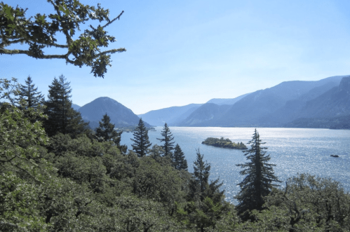 A scenic view of a river surrounded by mountains and lush trees under a clear blue sky.