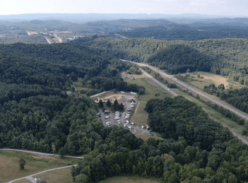 Aerial view of a wooded landscape with a small campground and highway in the distance, surrounded by rolling hills.
