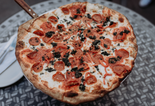 A freshly baked pepperoni pizza with a crispy crust, topped with melted cheese and black olives, on a metal table.