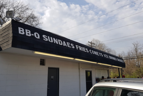 Sign on a building reads "BB-Q Sundaes Fries Coneys Ice Drinks Snacks" with a cloudy sky in the background.
