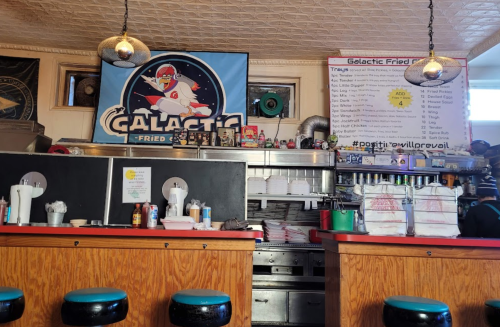 A retro diner interior featuring a "Galactic Fried" banner, colorful stools, and a menu on the wall.