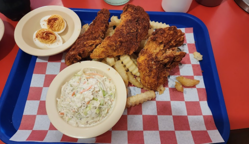 A blue tray with fried chicken, crinkle-cut fries, coleslaw, and deviled eggs on a checkered paper background.