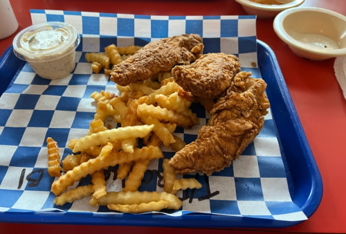 A blue tray with crinkle-cut fries and three pieces of fried chicken, accompanied by a small cup of dipping sauce.