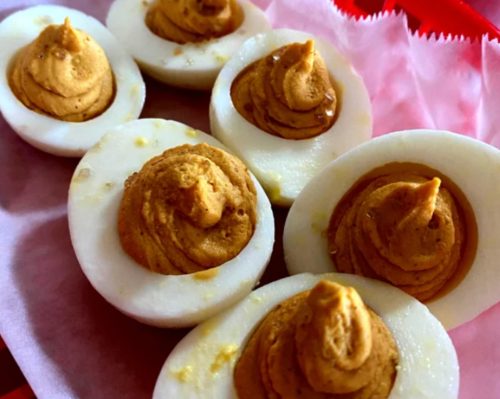 A close-up of deviled eggs topped with a creamy, golden filling on a pink paper liner.