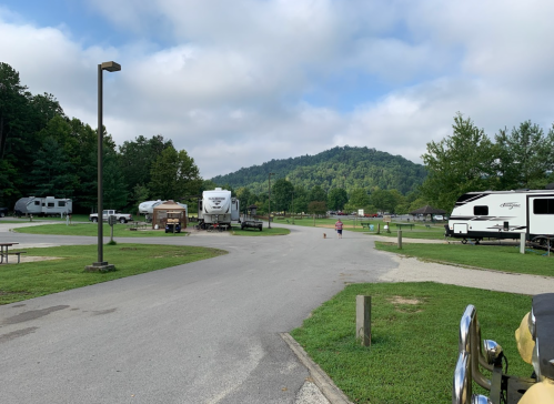 A scenic RV park with grassy areas, parked trailers, and a backdrop of rolling hills under a cloudy sky.
