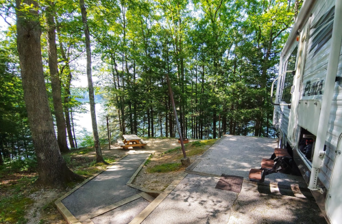A serene campsite with a picnic table by a lake, surrounded by lush trees and a parked RV.