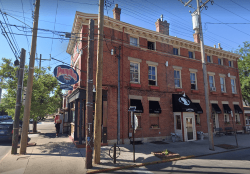 A brick building with a sign for "Pommie's Lounge," surrounded by trees and power lines on a sunny day.