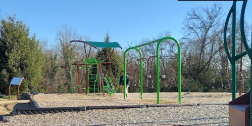 A playground with green equipment, including swings and climbing structures, set in a sunny outdoor area.