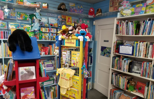 A cozy children's bookstore filled with colorful books, toys, and plush animals on shelves and displays.