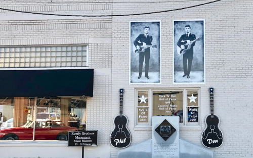 A brick wall features two large photos of musicians, guitars, and plaques for the Rock 'n' Roll Hall of Fame.