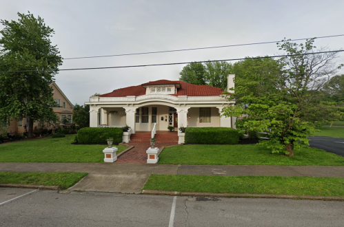 A charming white house with a red roof, surrounded by greenery and a well-maintained lawn.