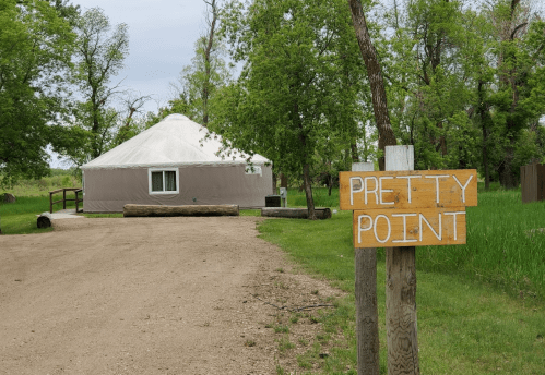 A yurt at Pretty Point, surrounded by trees and grass, with a gravel path leading to it.