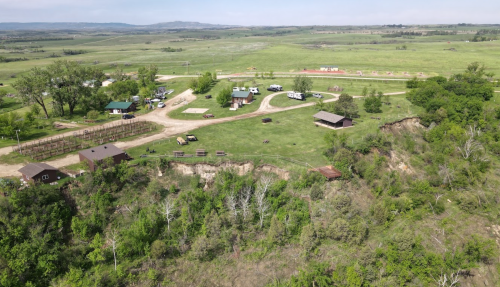 Aerial view of a rural landscape with green fields, a small settlement, and a cliff edge surrounded by trees.
