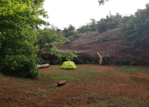 A bright green tent set up in a grassy clearing surrounded by trees and rocky terrain.