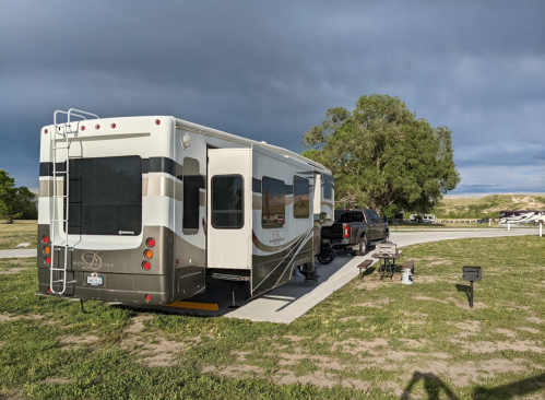 A parked RV with a truck nearby, set against a cloudy sky and green grass in a campground.