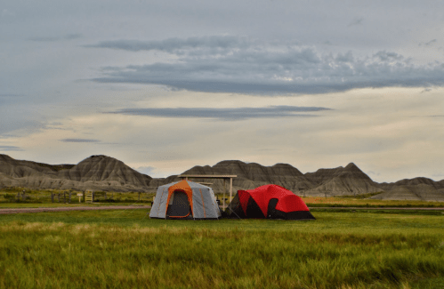 Two tents set up on grassy ground with rolling hills in the background under a cloudy sky.