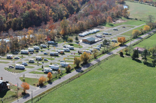 Aerial view of a campground with several RVs parked, surrounded by autumn foliage and green fields.