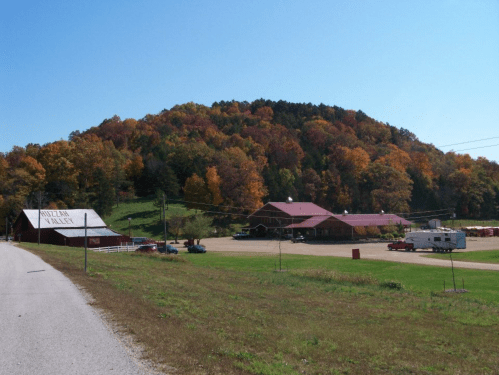 A scenic view of a rural area with a red barn, a building, and colorful autumn trees on a hillside under a clear blue sky.