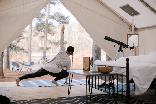 A person practicing yoga in a tent, with a telescope and outdoor scenery visible through the open entrance.