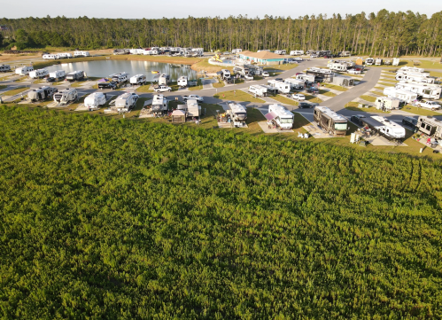 Aerial view of a campground with RVs parked near a pond, surrounded by green fields and trees.