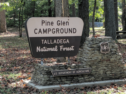 Sign for Pine Glen Campground in Talladega National Forest, featuring stone base and U.S. Department of Agriculture emblem.
