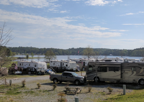 A scenic view of a lakeside RV park with several parked RVs and a calm water backdrop under a blue sky.