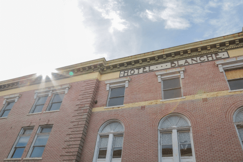 Historic building with a sign reading "Hotel Blanche," featuring brick architecture and sunlight in the background.