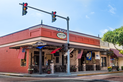 A brick building with flags and outdoor seating, located at a street corner with traffic lights.