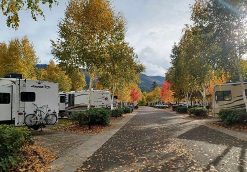 A scenic RV park lined with trees in autumn colors, featuring parked RVs and a bike on a path.