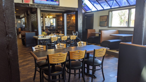 Interior of a restaurant featuring wooden tables, chairs, and booths, with natural light coming through large windows.