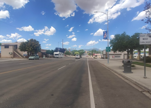 A wide street with a clear sky, trees, and buildings on either side, featuring a sign for right turn instructions.