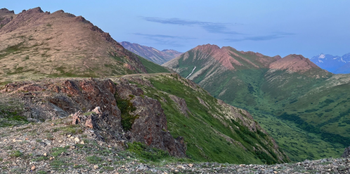 A panoramic view of rugged mountains with green slopes under a clear blue sky.