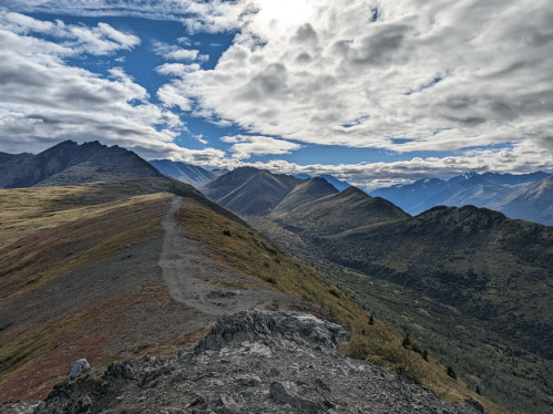 A scenic mountain landscape with a winding path, under a partly cloudy sky and vibrant green and brown terrain.