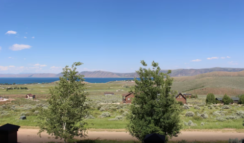 Scenic view of a lake surrounded by green hills and trees under a clear blue sky.